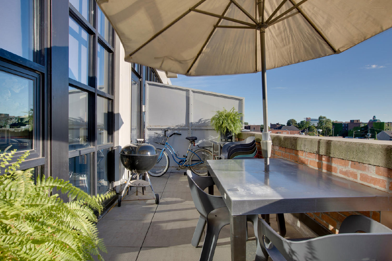 Outdoor balcony with table, chairs, umbrella, bicycle, and BBQ grill of a Detroit Canfield apartment.